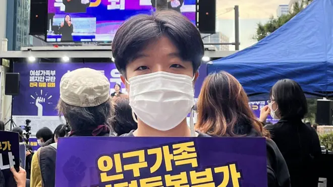 在一場抗議活動中，一名戴著口罩的女性高舉一個寫有韓文的標語牌。