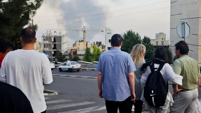 People stand with their backs to the camera as they look at smoke rising in the horizon in Tehran on Monday