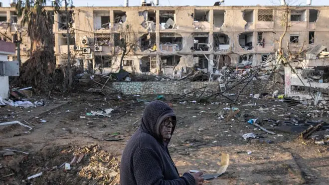 Мужчина пьет кофе, глядя на дома, разрушенные в результате ракетного удара Ирана по Димоне 22 марта 2026 года.