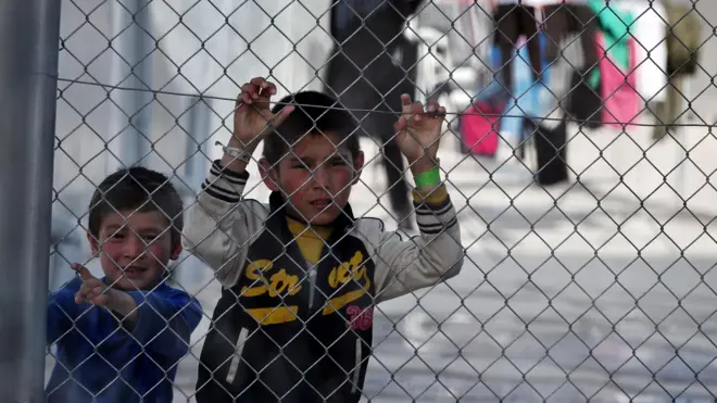 Два мальчика за сетчатым забором центра сбора беженцев