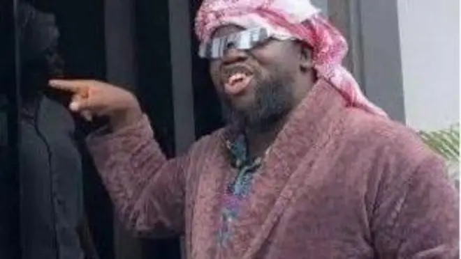 Mama Deola asọ obinrin, we gele, to si n kan ilẹkun kan.
