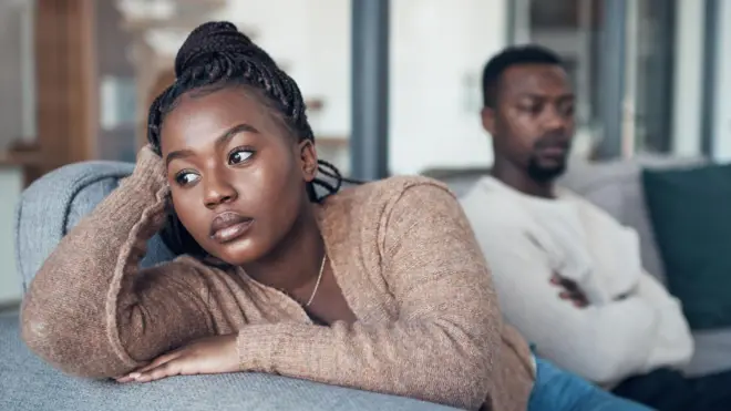 Une femme qui a l'air triste avec un homme qui croise les bras en arrière-plan