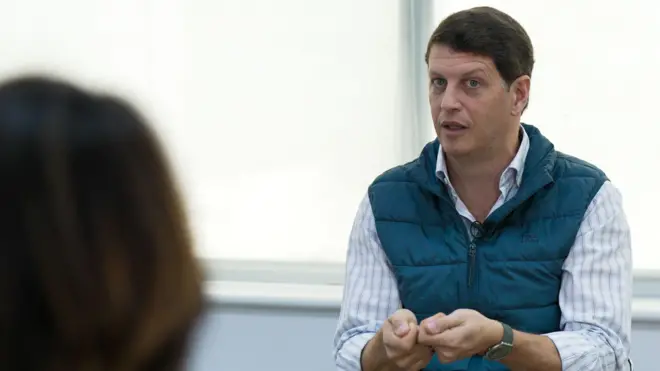 Foto de Ricardo Salles, vestindo uma camisa azul listrada e um colete azul por cima. 