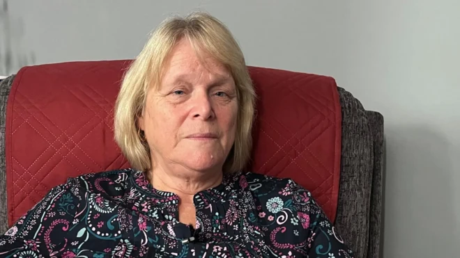 Ifoto y'umugore usa n'unaniwe, wambaye ishati y'amabara menshi, aho yicaye mu ntebe yegamye