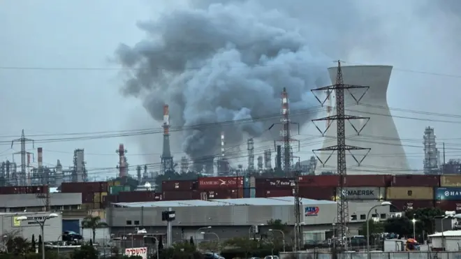 ईरान के साथ अमेरिका-इसराइल संघर्ष के बीच, 19 मार्च, 2026 को इसराइल के हाइफा में एक तेल रिफाइनरी से धुआं उठ रहा है, जो ईरानी हमले में क्षतिग्रस्त हो गई थी.