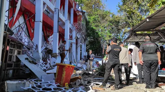 Solda kısmen yıkılmış bir bina, sağda 5-6 yetkili. Havanın güneşli, ılık olduğu anlaşılıyor. 