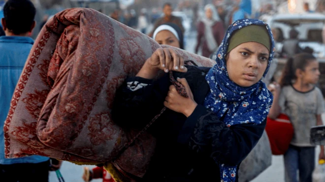 Una mujer carga un colchón mientras camina por una calle de Gaza completamente destruida. 