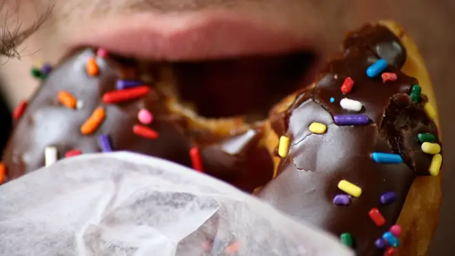 Close up of a man eating a chocolate doughnut with colourful sprinkles