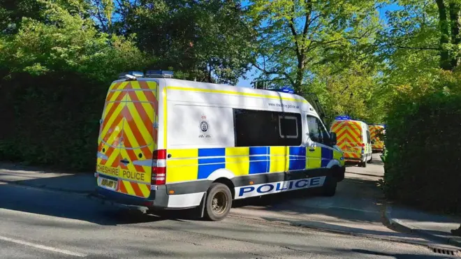 Three police vans in a row, parked in a a small side road. There are trees either side of the road.