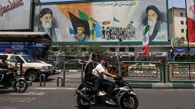 يمر إيرانيون أمام لافتة تحمل صورة المرشد الأعلى الإيراني الراحل آية الله روح الله الخميني (يمين) وخليفته الراحل آية الله علي خامنئي (يسار) في ساحة انقلاب بطهران في 3 يونيو/حزيران 2026.