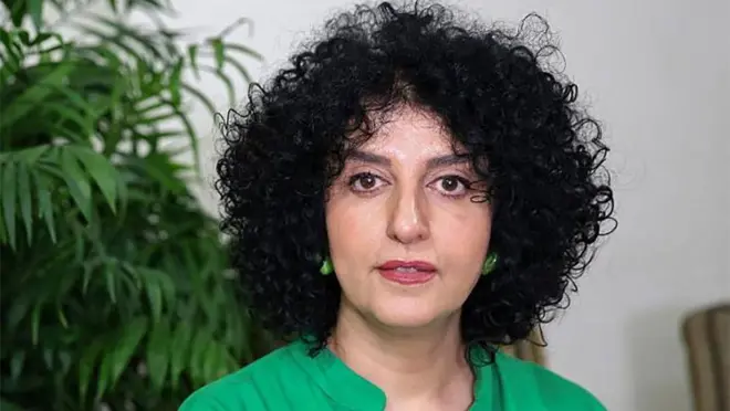 緑の服を着たイランの人権活動家モハンマディ氏が、テヘランの自宅アパートの椅子に座り、口を少し開いてカメラを見つめている