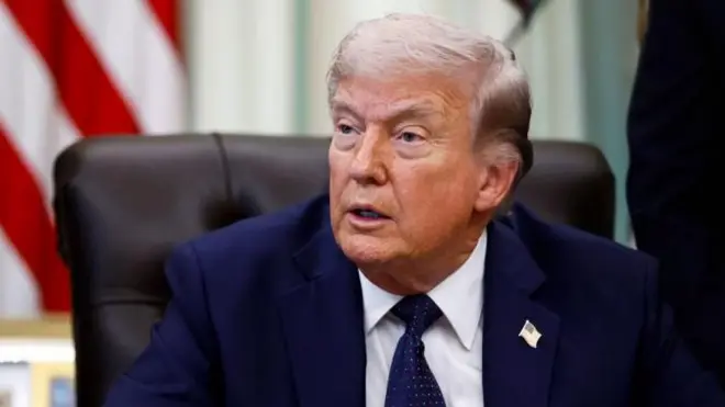 ダークスーツ姿のトランプ氏がいすにすわり、斜めを向いて口を開いている