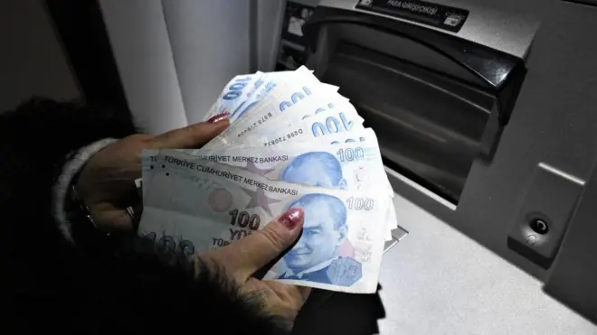 Bankamatik önünde Türk Lirası banknotları tutan bir el.