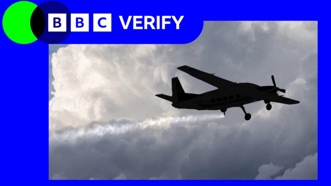 بادلوں میں اڑتا ایک چھوٹا طیارہ آسمان میں باریک ذرات کا چھڑکاؤ کر رہا ہے، پیچھے ایک لمبی سفید لکیر بن رہی ہے۔ اوپر بائیں کونے میں بی بی سی ویریفائی کا لوگو دکھائی دیتا ہے۔