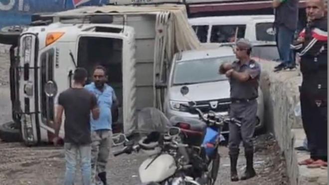 مواطنون وعنصر من الدرك اللبناني يقفون بجوار الشاحنة المقلوبة
