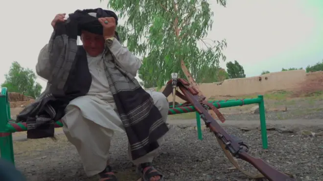 Ҳукмина ўриндиқда бошига салла ўраяпти, ёнида милтиғи турибди