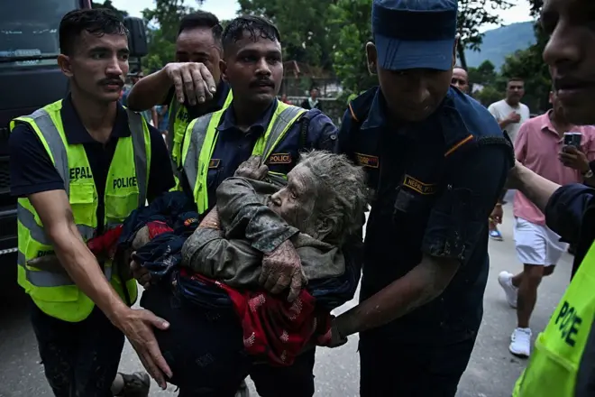 Rescuers carry in their arms a flood survivor, following flash floods and a landslide disaster in Devghat, in the Nepal's Nuwakot district on August 26, 2026. A massive flood and landslide disaster on the Nepal-Tibet border killed at least 103 people on August 26, 2026 and left several hundred missing, many of them foreign tourists. Aid workers said entire settlements had been "wiped out". Some 403 tourists -- 341 of them foreigners -- were unaccounted for several hours after the disaster struck, according to the tourism ministry. 