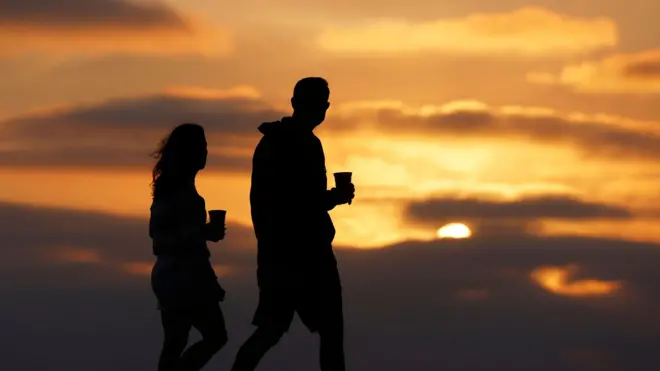 زوجان يتنزهان على طول ساحل لا جولا عند غروب الشمس في أمسية صيفية دافئة في 3 أغسطس/آب 2025 في سان دييغو، كاليفورنيا.