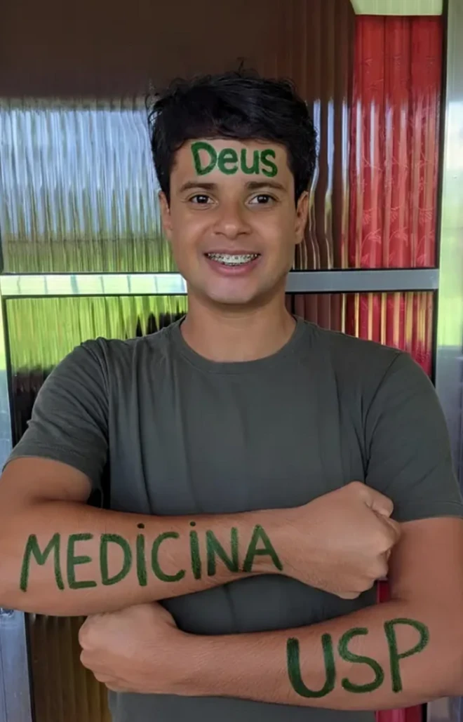 Wesley mostra os braços onde está escrito: Medicina USP. Na testa dele está escrito: Deus