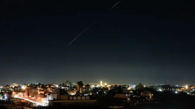 Umurongo w'igisasu mu kirere ca Israel mw'ijoro, hejuru y'inyubakwa nyinshi ziriko amatara
