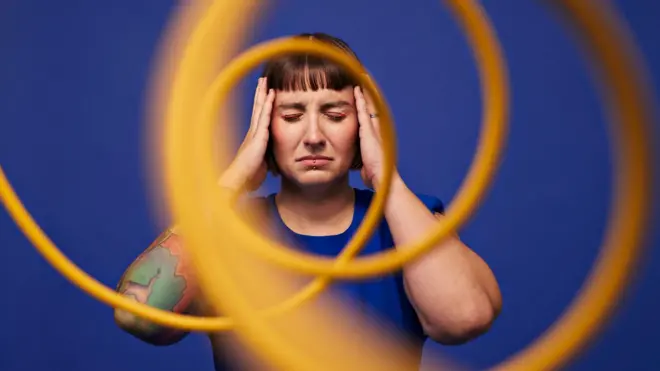Mujer con la cabeza entre las manos de pie con los ojos cerrados detrás de cables en espiral contra un fondo azul