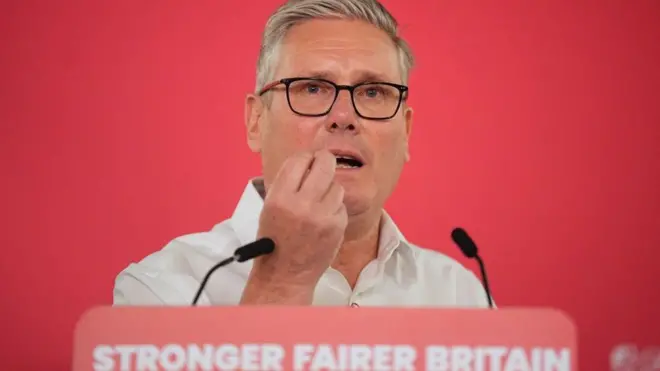 Starmer za govornicom ispred koje je tabla na kojoj je slogan: 'Jača i poštenija Britanija'