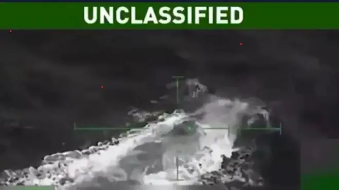 Imagen difuminada en blanco y negro en la que se percibe una especie de submarino que empieza a reflotar en el mar. 