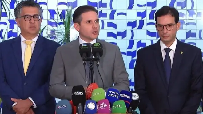 Três homens em frente a vários microfones