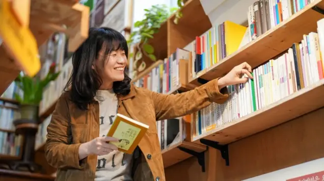 一个女性正在书架上找书，面带笑容。