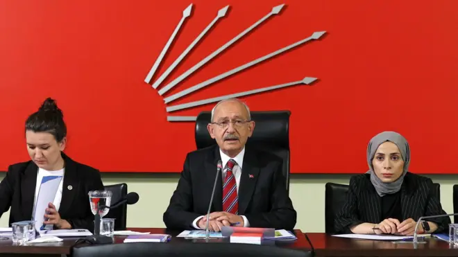 Kemal Kılıçdaroğlu ortada duruyor. Sol yanında başörtülü bir üye var, diğer tarafında ise başı açık bir kadın elindeki dosyaya baklıyor.
