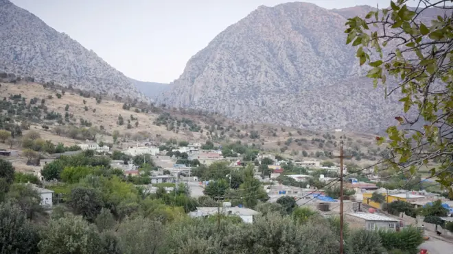 مشهد عام لقرية خلابة بمنازل ومبانٍ تتوسطها الأشجار والأراضي الزراعية، وتبدو الجبال في أفق القرية.