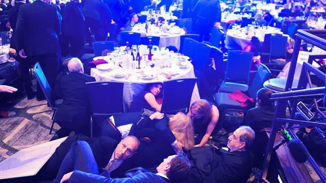 Abantu benshi bikinze munsi y'ameza menshi ariho ibyo kunywa no kurya, mu cyumba kirimo n'abandi bantu benshi, nyuma yuko amasasu yumvikanye muri Hoteli Hilton, mu isangira ry'abategetsi n'abanyamakuru batara amakuru muri White House, mu ijoro ryo ku wa gatandatu, ku itariki ya 25 Mata (4) mu 2026. 