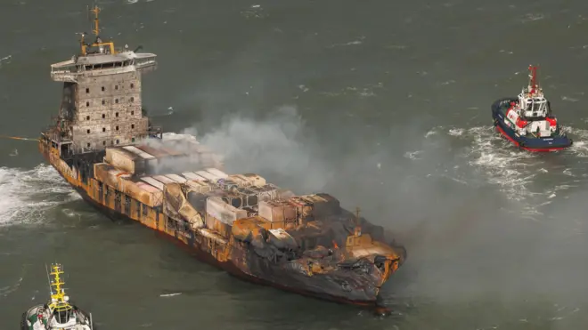 Фото сверху: дымящееся судно с поврежденным носом и два более мелких судна рядом