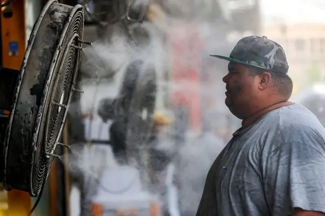 A man stands in front of a fan misting water in Baghdad where heat spiked to over 50 C or 122 F