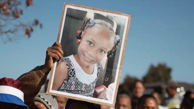 A picture of a young girl who is smiling is held to the sky among a crowd of people.