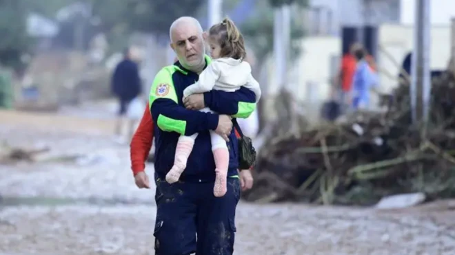 یک امدادگر کودکی را بغل کرده و از میان سیل عبور میکند