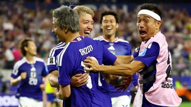 青色ユニホームの前田がチームメートと抱き合って笑顔を見せている。他の日本選手らも近くで笑顔を見せている
