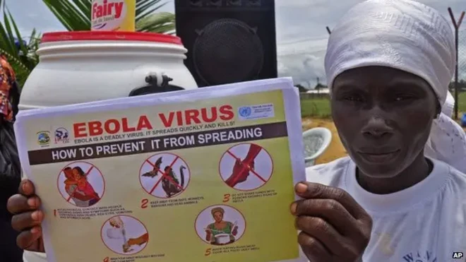 Людина тримає плакат «Ebola virus» із правилами профілактики поширення, поруч засоби гігієни.

