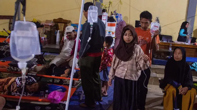 Pasien korban keracunan massal berjalan dengan infus terpasang saat mendapatkan perawatan di Posko Penanganan Kantor Kecamatan Cipongkor, Kabupaten Bandung Barat, Jawa Barat, Jumat (26/9/2025).