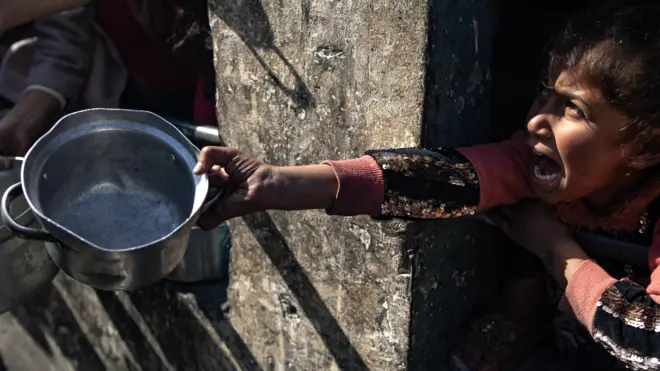 A displaced Palestinian child holds up an empty pot 
