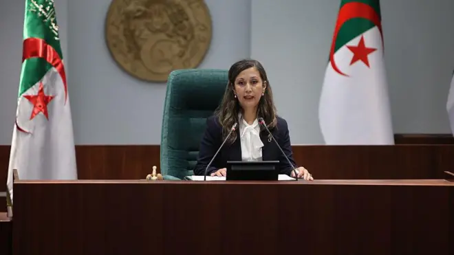 خليدة بوفدش على كرسي رائسة مجلس الشعب تلقي كلمة وبجانلها علم الجزائر