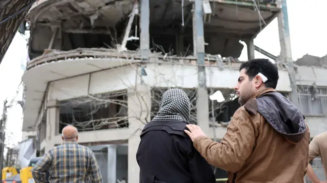 Moradores reagem à sua residência danificada ao lado de um prédio comercial que inclui escritórios da emissora qatari Al Araby TV, após um ataque aéreo no norte de Teerã