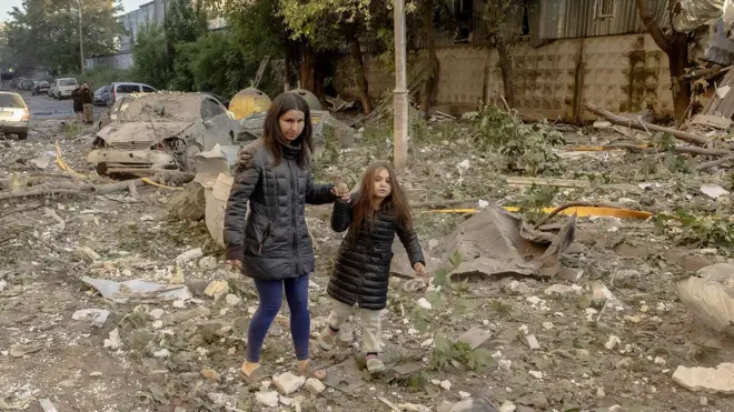 A primera hora de la mañana, una mujer y una niña pequeña caminan de la mano sobre una zona de escombros y escombros en Kyiv