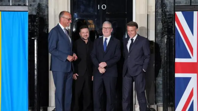 ウクライナやイギリスの国旗が左右に並ぶ首相官邸の黒い玄関扉を前に、メルツ独首相、ゼレンスキー・ウクライナ大統領、スターマー英首相、マクロン仏大統領が笑顔で並んでいる
