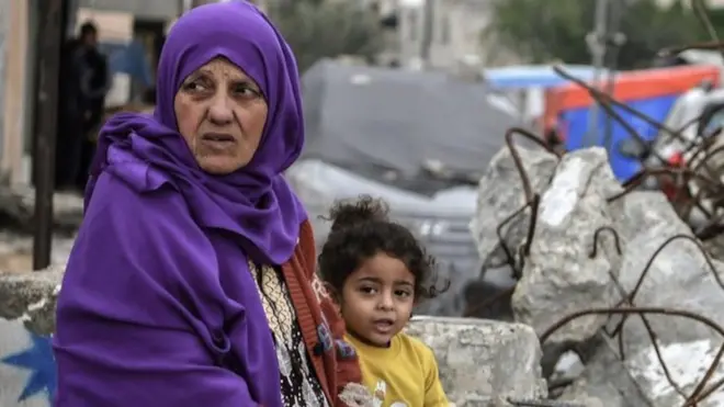 身穿紫色披肩的婦女和小孩坐在拉法的廢墟中。