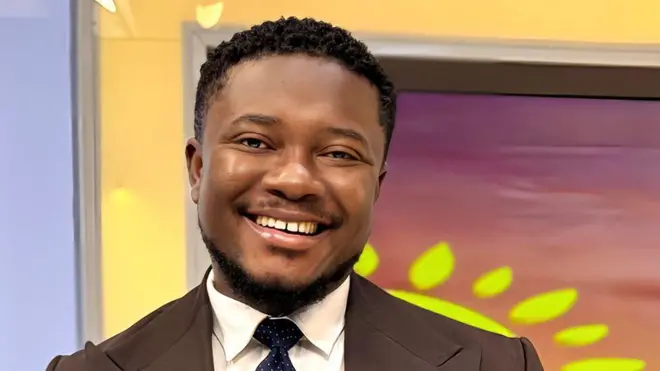 Aworan Godwin Asediba, lati ori de ejika rẹ. O gẹ irun ori rẹ lọ silẹ, irungbọn rẹ naa ko si gùn pẹlu. O n rẹ́rìn-ín, o si n wo oju kamẹra lọọkan.