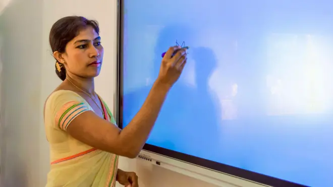 තරුණ ගුරුවරියක් ස්මාර්ට් බෝඩ් එකක් මත ලියයි