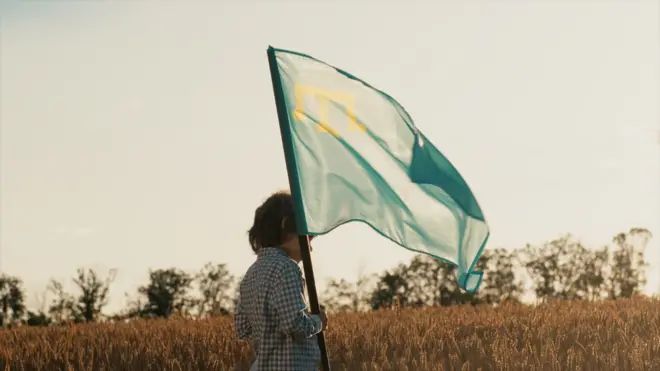 Kırım Özerk Cumhuriyeti Bayrağı'nı taşıyan bir kişi, bir tarlada başakların arasında yürüyor