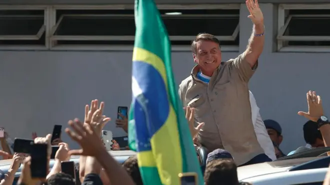 Bolsonaro sorrindo acena para apoiadores diante7upbet linkbandeira do Brasil