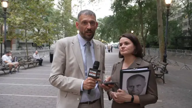 Сергей и Светлана Тихановские в Нью-Йорке в сентябре 2025 года. Сергей в светлом бежевом костюме, светло-голубой рубашке и сером галстуке держит микрофон с символикой своего канала "Страна для жизни". Светлана в серо-бежевом костюме держит в руках портрет политзаключенного и отвечает на вопросы своего мужа.